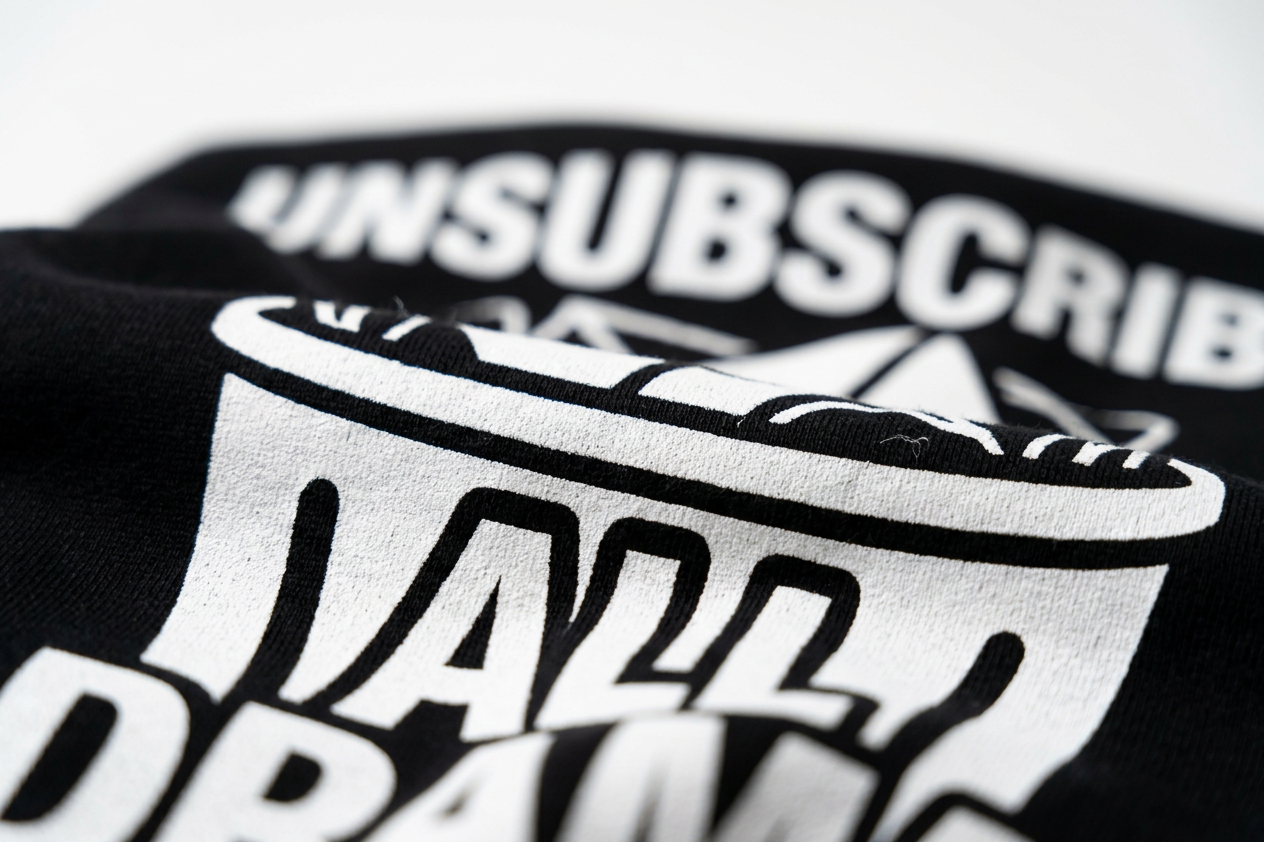 Close-up of a black hoodie, featuring a bold white graphic print with the word 'UNSUBSCRIBE' and stylized lettering.