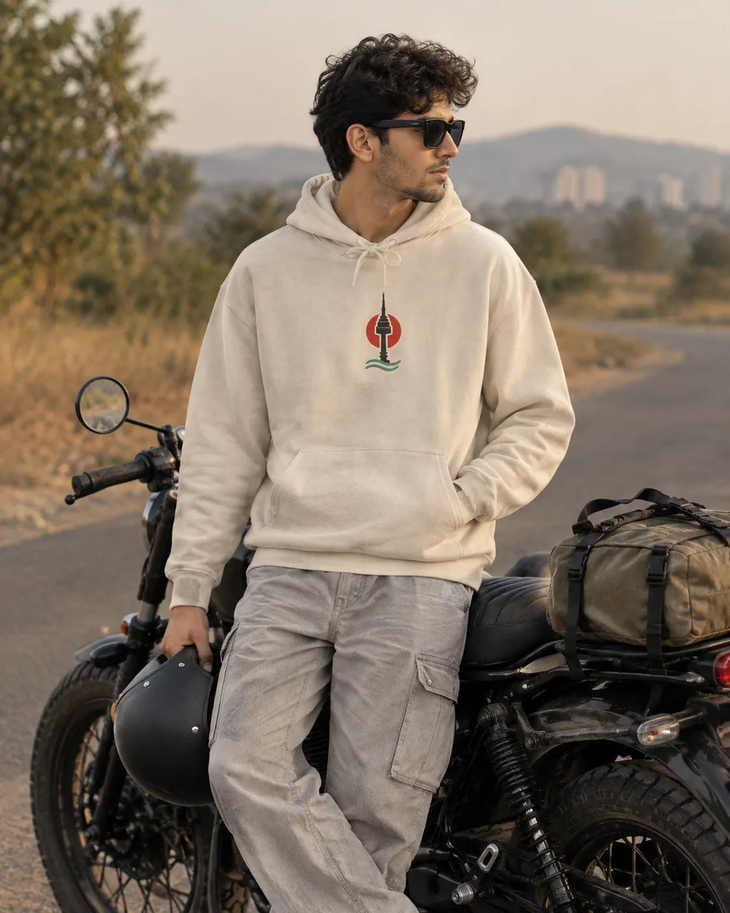 Man in a beige Seoul Mate Korean hoodie with a small front chest print, standing by a black motorcycle on an open highway