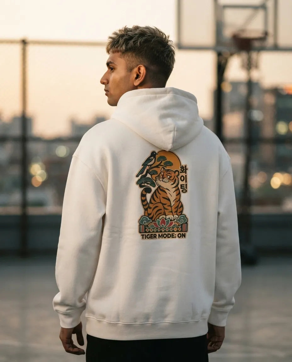 Man standing on an outdoor basketball court at sunset, wearing an off-white Tiger Mode On Korean hoodie with a tiger back print