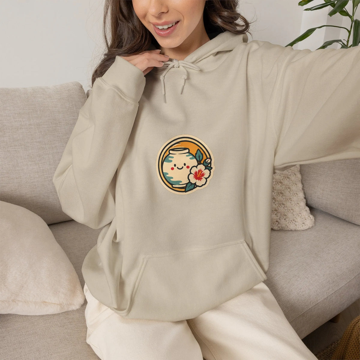 Woman sitting on a sofa in a beige hoodie with a round chest print