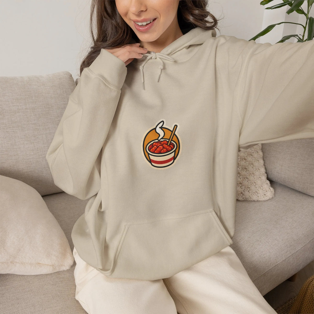 Woman sitting on a sofa in a beige hoodie with a small tteokbokki print