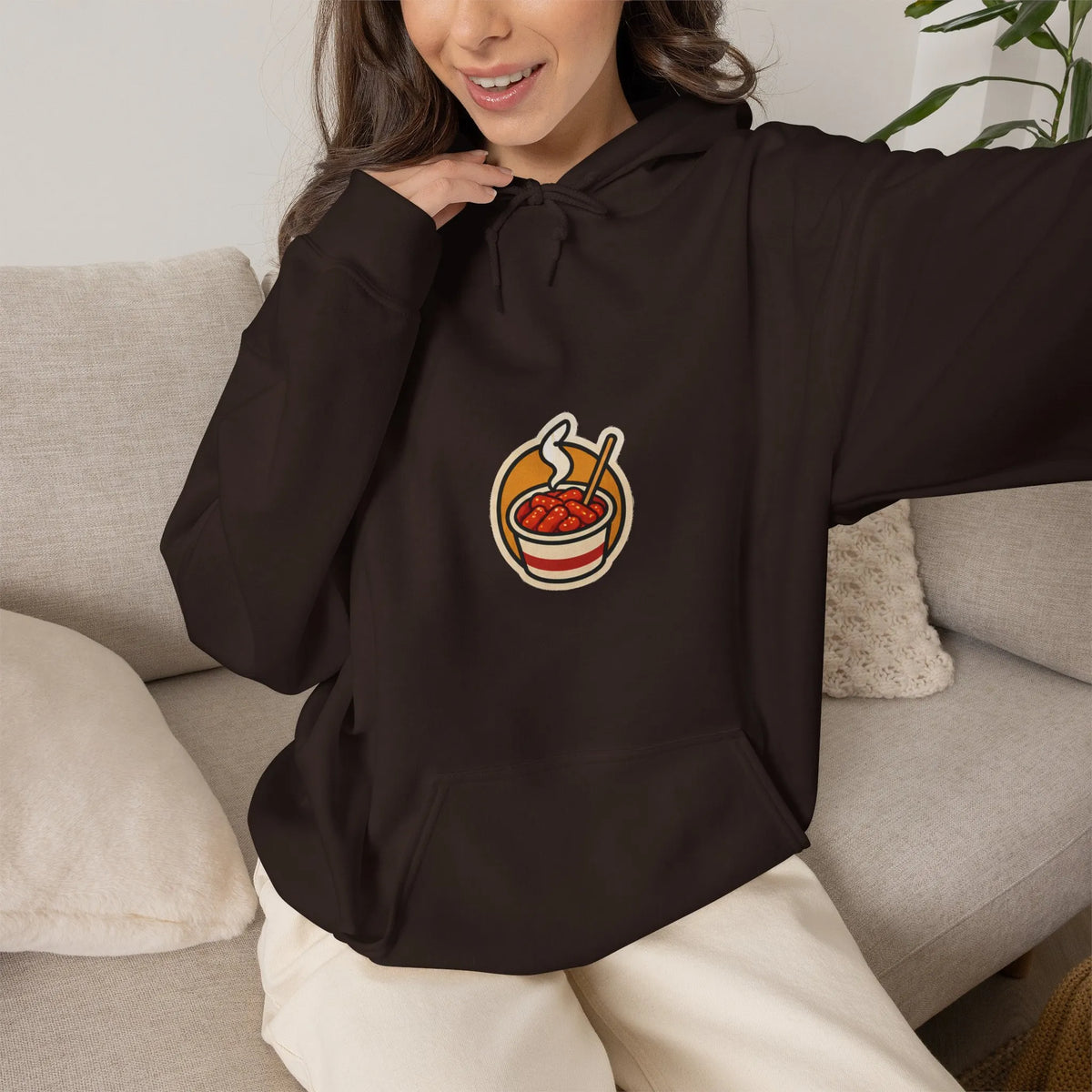 Woman relaxing on a sofa in a coffee brown hoodie with a small tteokbokki print