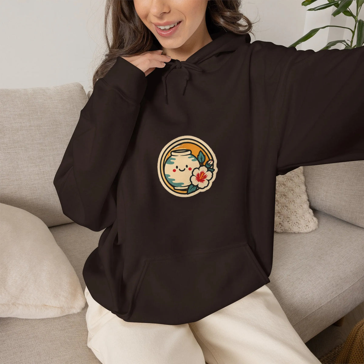 Woman on a sofa in a coffee brown hoodie with a round badge print on the chest