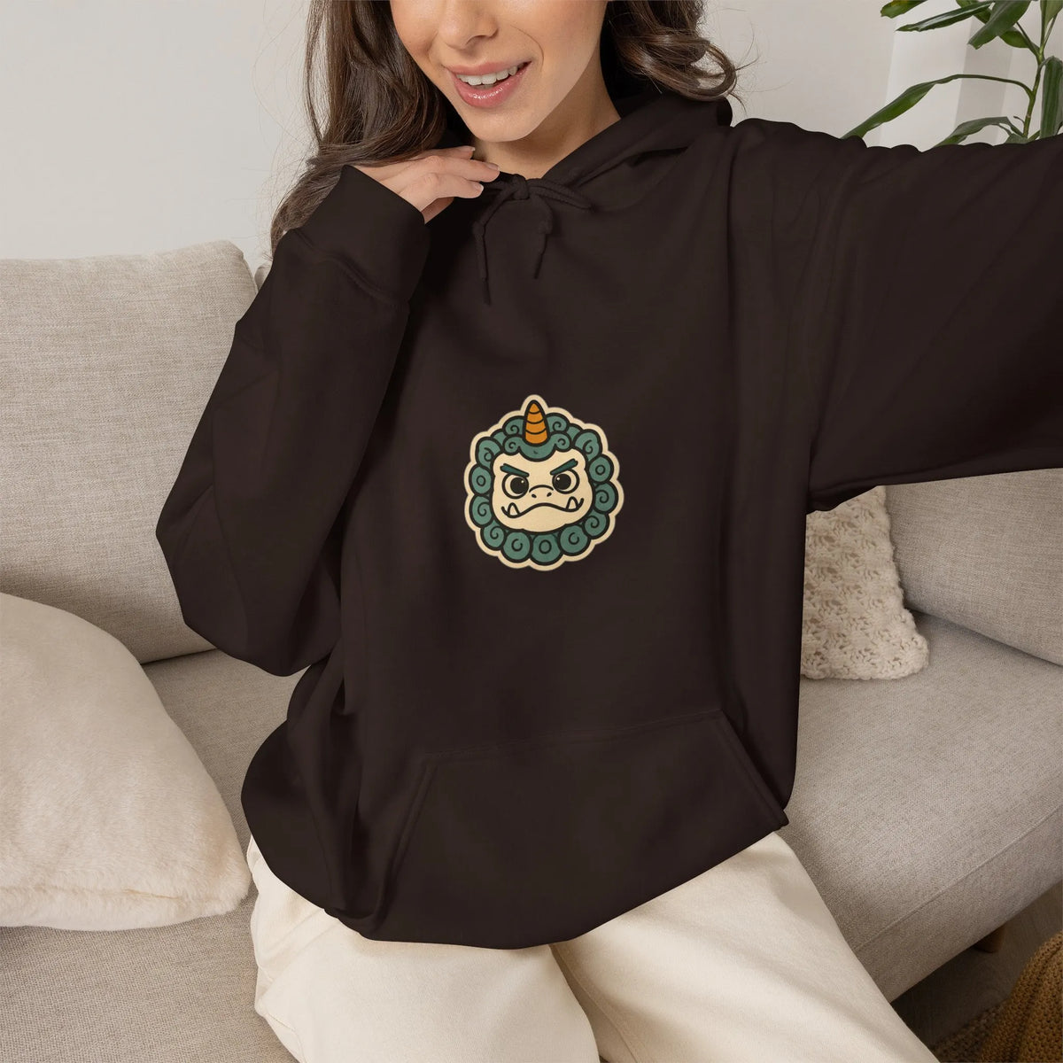 Woman on a sofa in a coffee brown hoodie with a small grumpy haetae badge