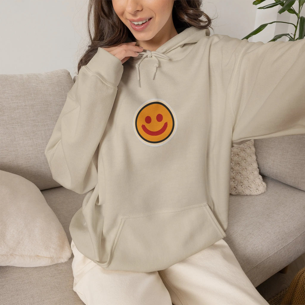 Woman on a sofa in a beige hoodie with a small smiley face print
