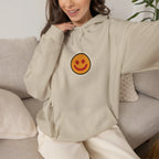 Woman on a sofa in a beige hoodie with a small smiley face print