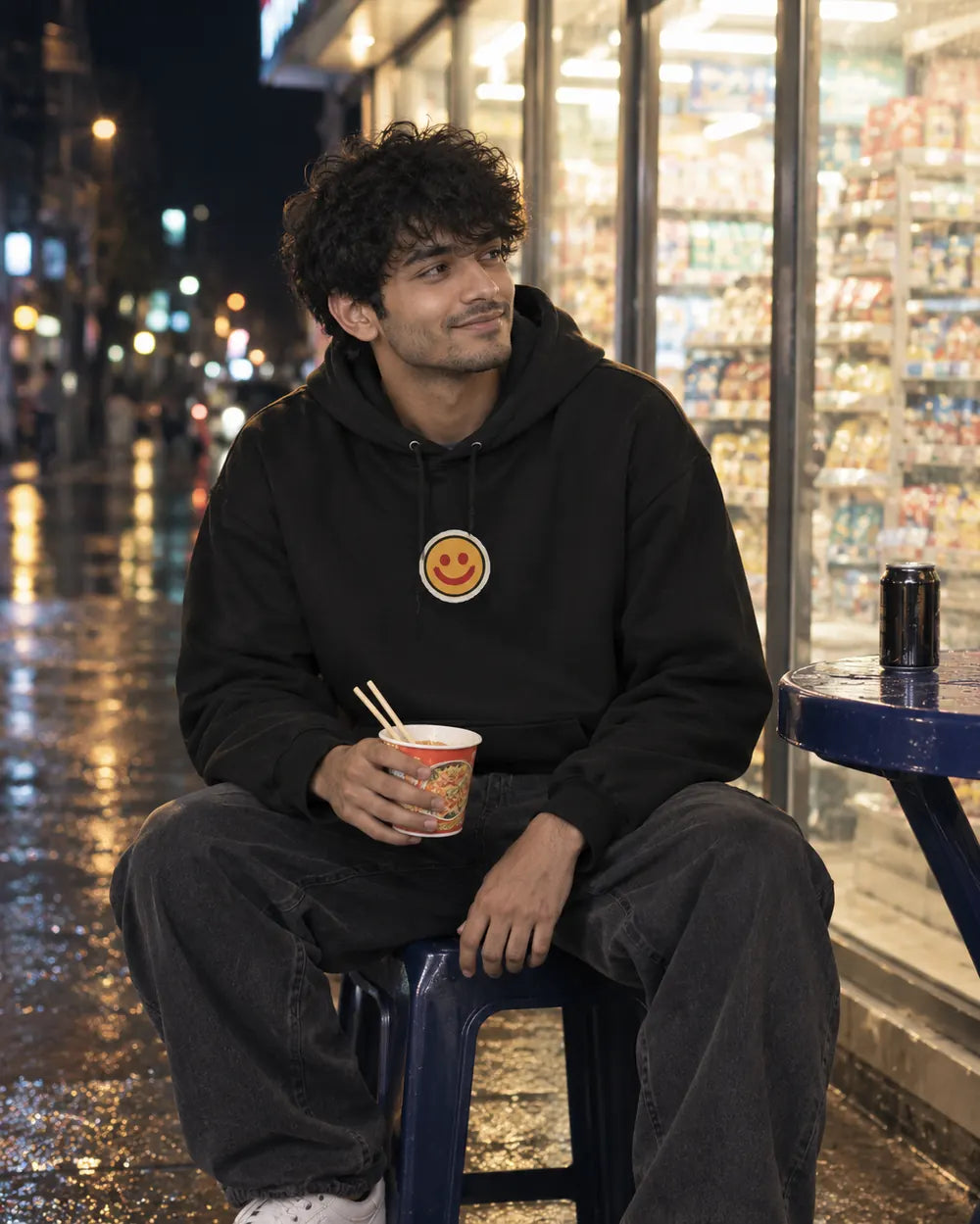 Man in a black I'm Fine Korean hoodie eating cup ramen outside a convenience store at night