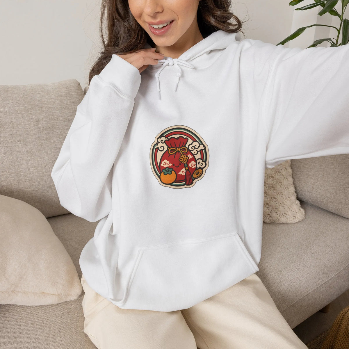 Woman on a sofa in an off-white hoodie with a small lucky pouch badge on the chest