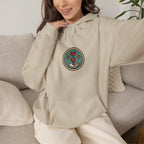 Woman on a sofa in a beige hoodie with a small round gaming badge on the chest