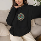 Woman sitting on a sofa in a black hoodie with a small round gaming badge
