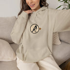Woman on a sofa in a beige hoodie with a small round athletic badge on the chest
