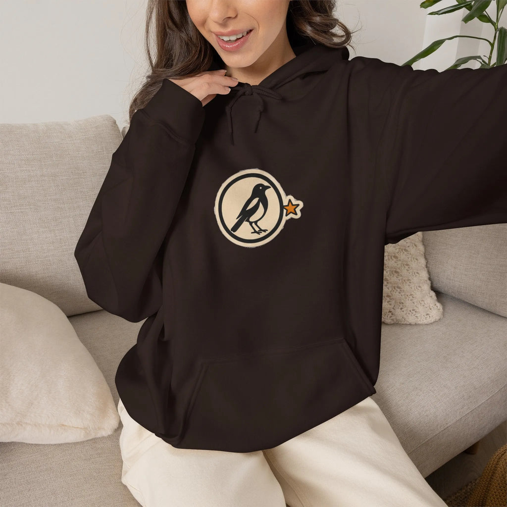 Woman on a sofa in a coffee brown hoodie with a small round athletic badge
