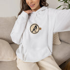 Woman sitting on a sofa in an off-white hoodie with a small round athletic badge