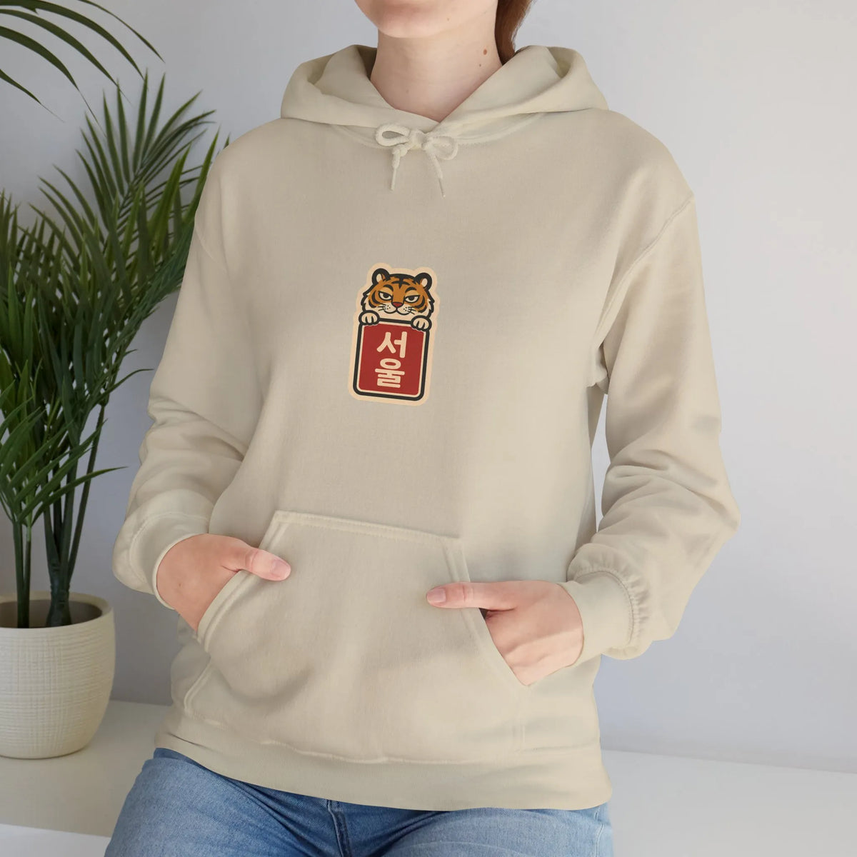 Woman standing at home in a beige hoodie with hands in the pocket