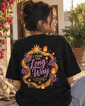 Woman wearing a black oversized Wear Pardesi t-shirt with an "I Took the Long Way" back print framed by golden braids and flowers