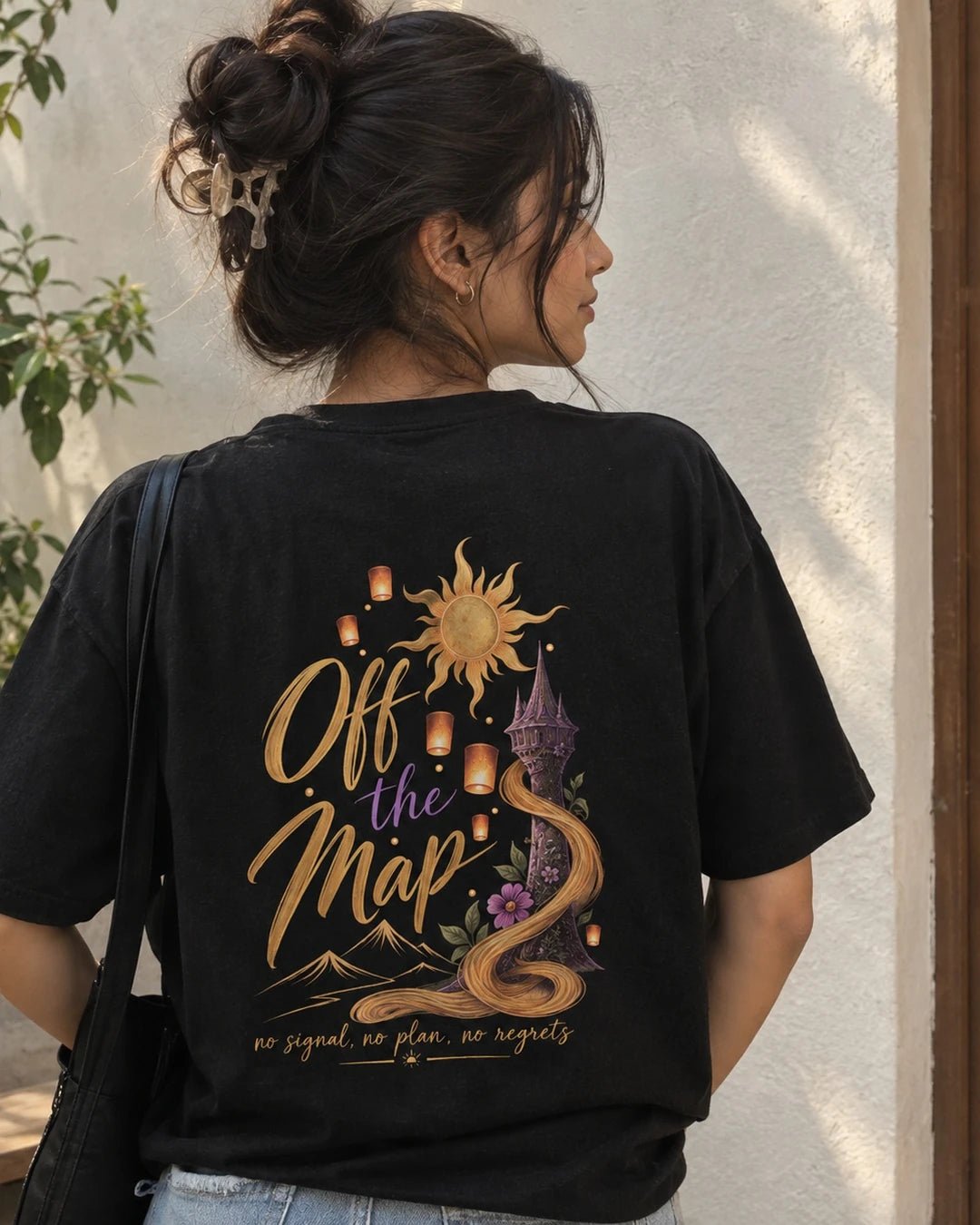 Woman wearing a black oversized Wear Pardesi t-shirt with an "Off the Map" back print, a golden sun, lanterns and a purple tower